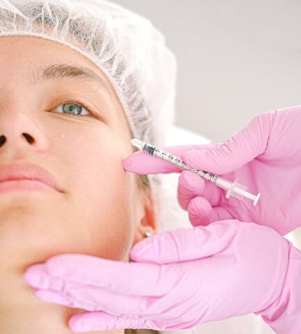 Close-up of a beautician administering facial injection treatment to a woman in a clinical setting.